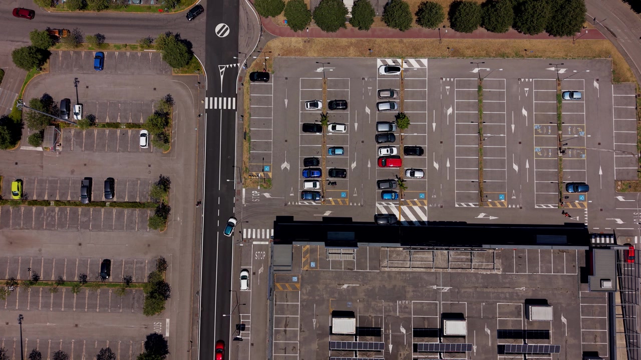 Vista aérea del estacionamiento de un centro comercial con estaciones de carga para vehículos eléctricos y paneles solares en el tejado, apoyando soluciones energéticas urbanas sostenibles