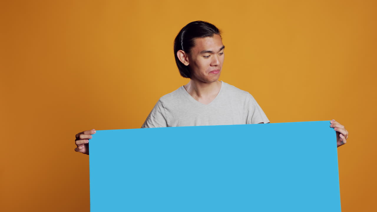 Asian young man holding blue carton board on camera