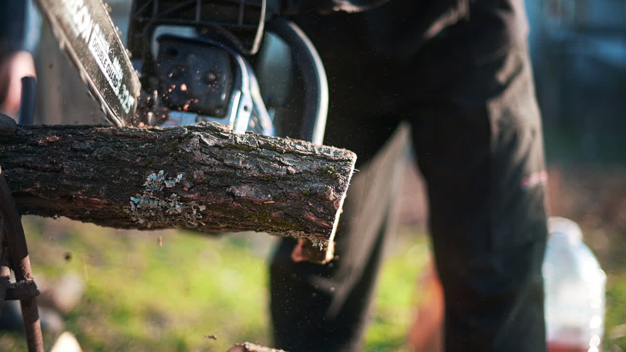 Man in gloves is choping wood using a chainsaw. Close view