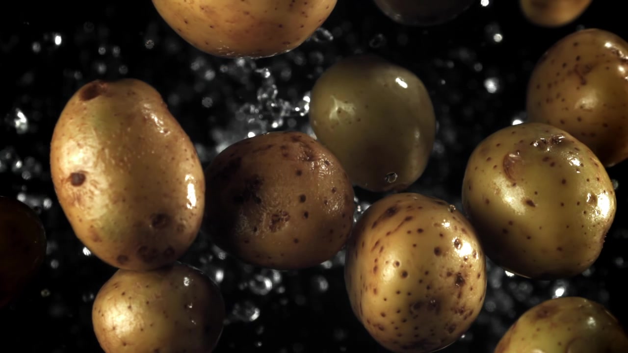 Patate fresche che cadono con gocce d'acqua su sfondo nero