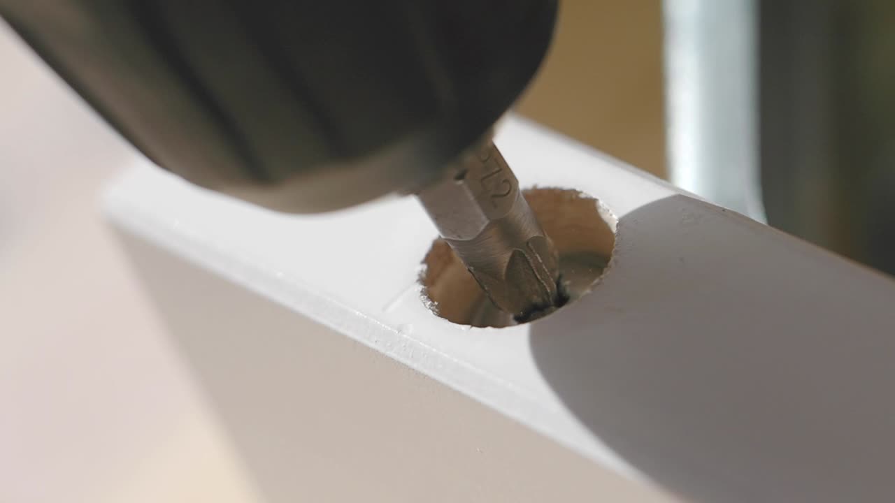 Drilling a screw into a white wooden furniture component