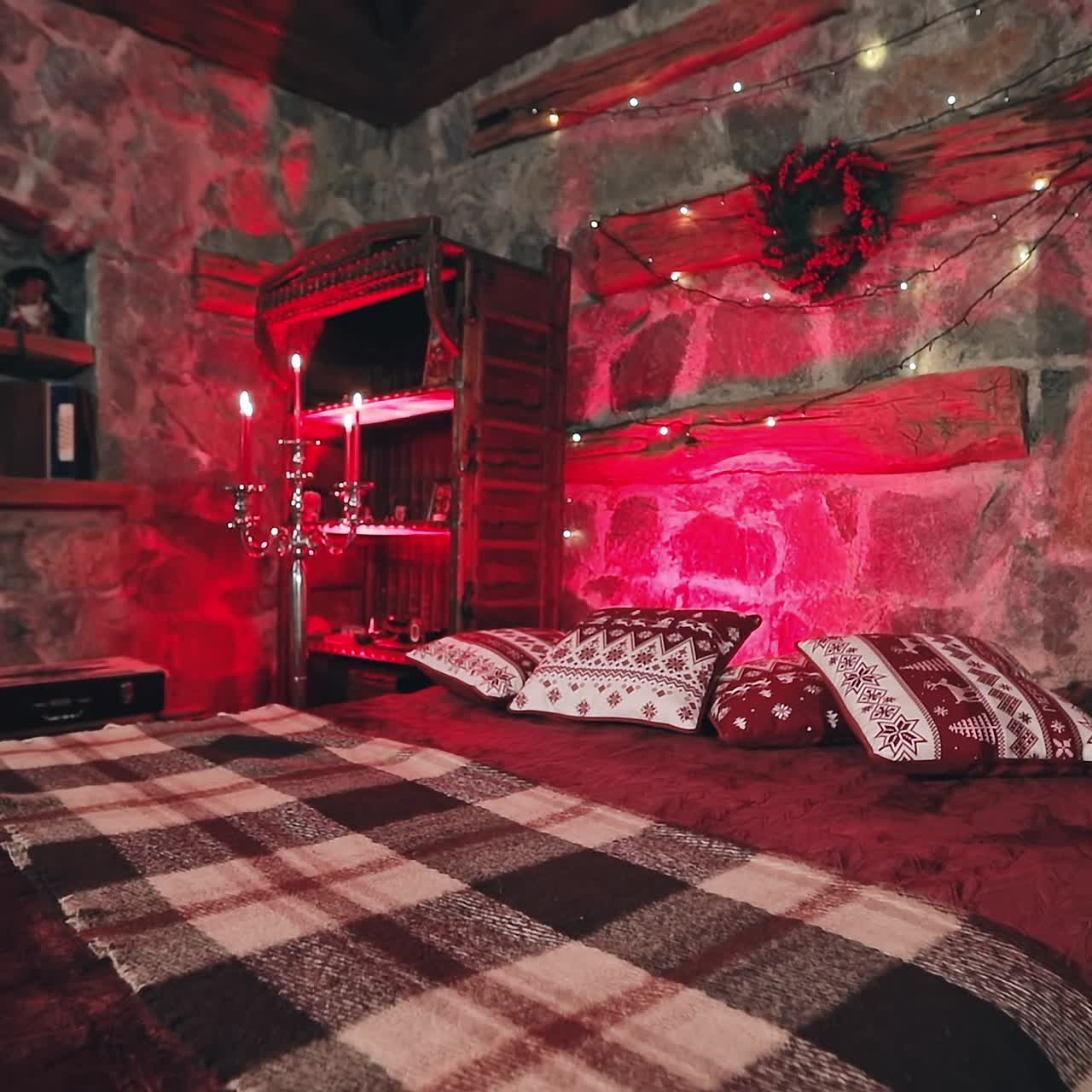 Romantic bedroom at Christmas. Cozy bed and Christmas garland on a wall. Candlesticks with red candles. Christmas decor in the room. Red lighting