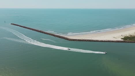 aerial tracking shot of speedboats cruising into river mouth coming from blue ocean