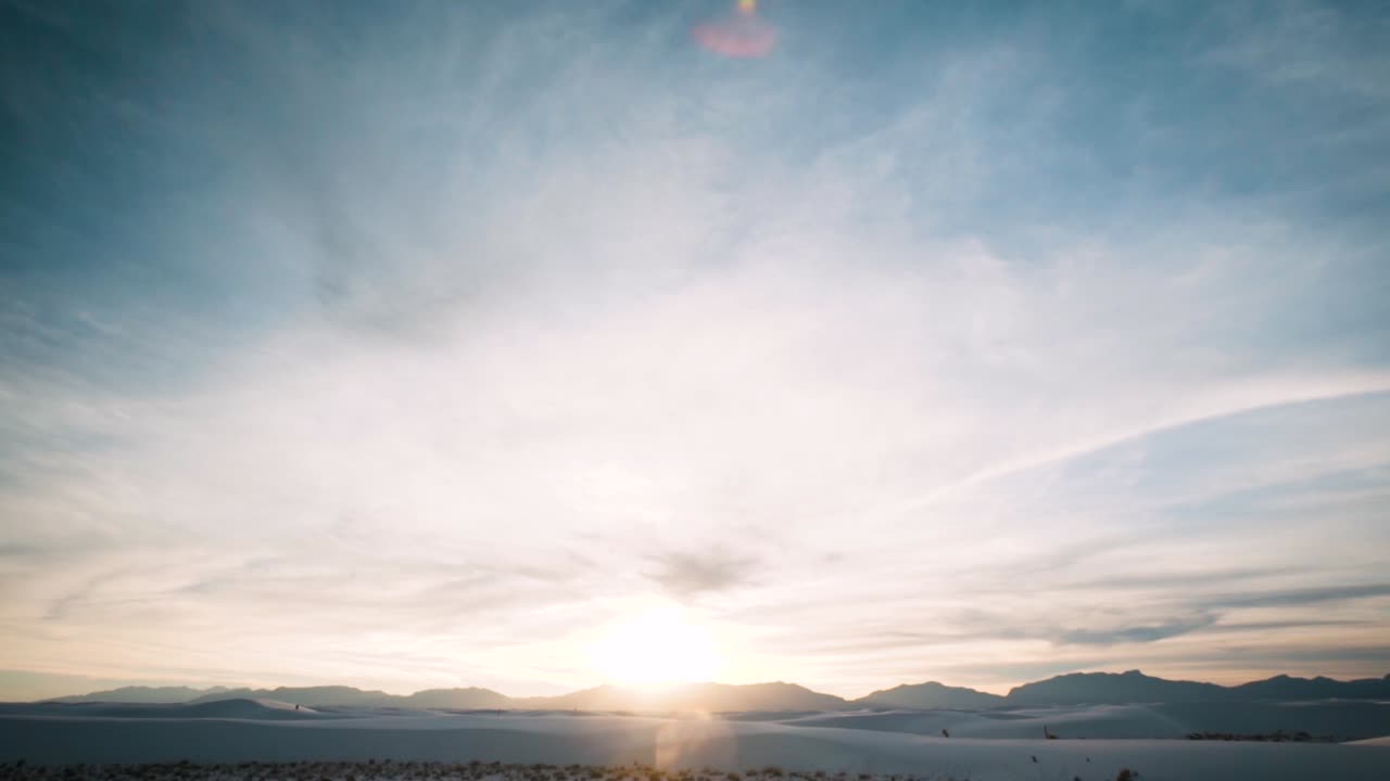 Sunset over mountain range at white sand dunes covered in footprints