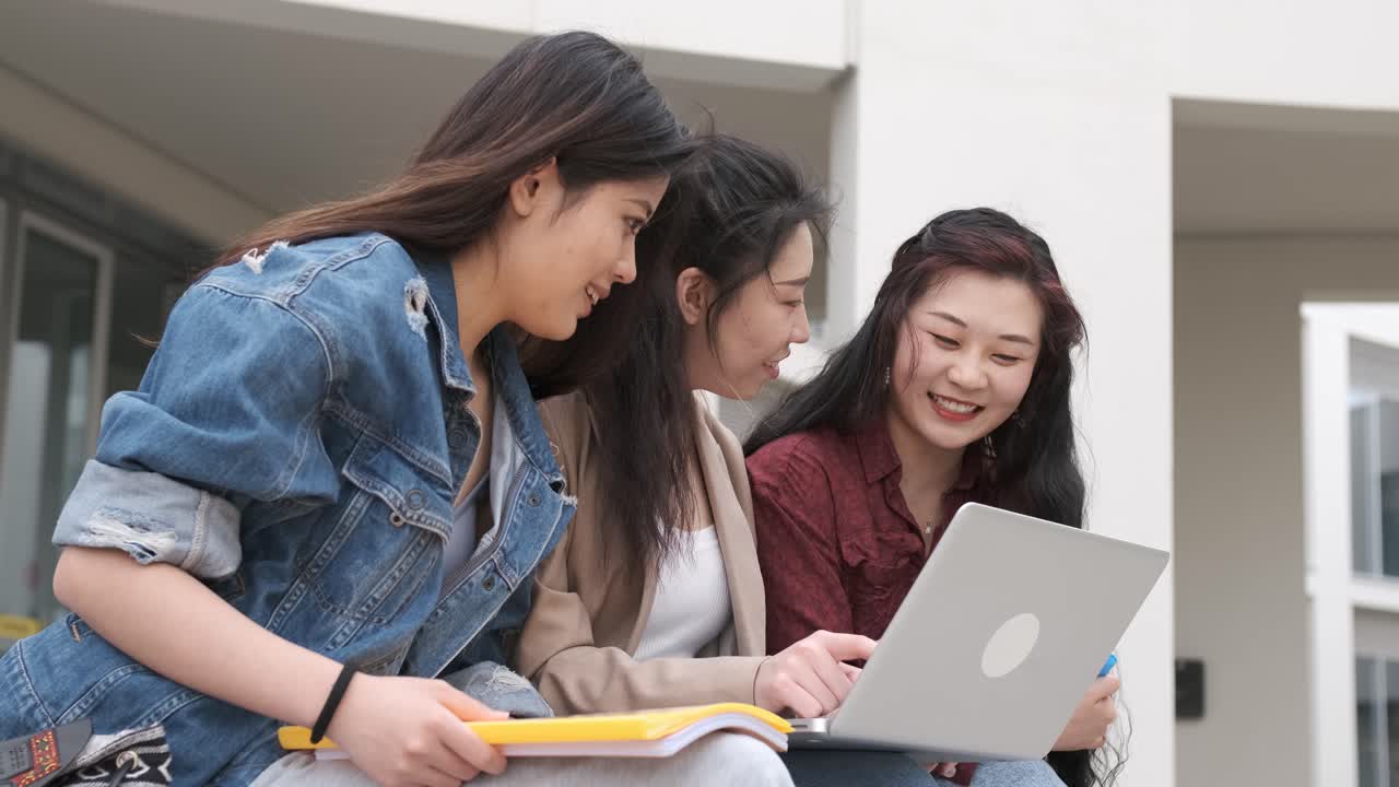三名亞洲女學生在休息時間坐在校園裡使用手提電腦。