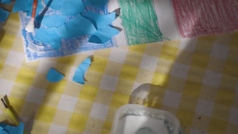 crafting session with torn blue paper and glue on a checkered tablecloth