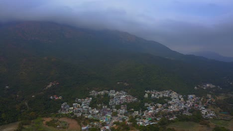 toma de drones de un antiguo pueblo pequeño en la parte inferior de una montaña con un bosque durante el día, las nubes se pegan a la cima de la montaña