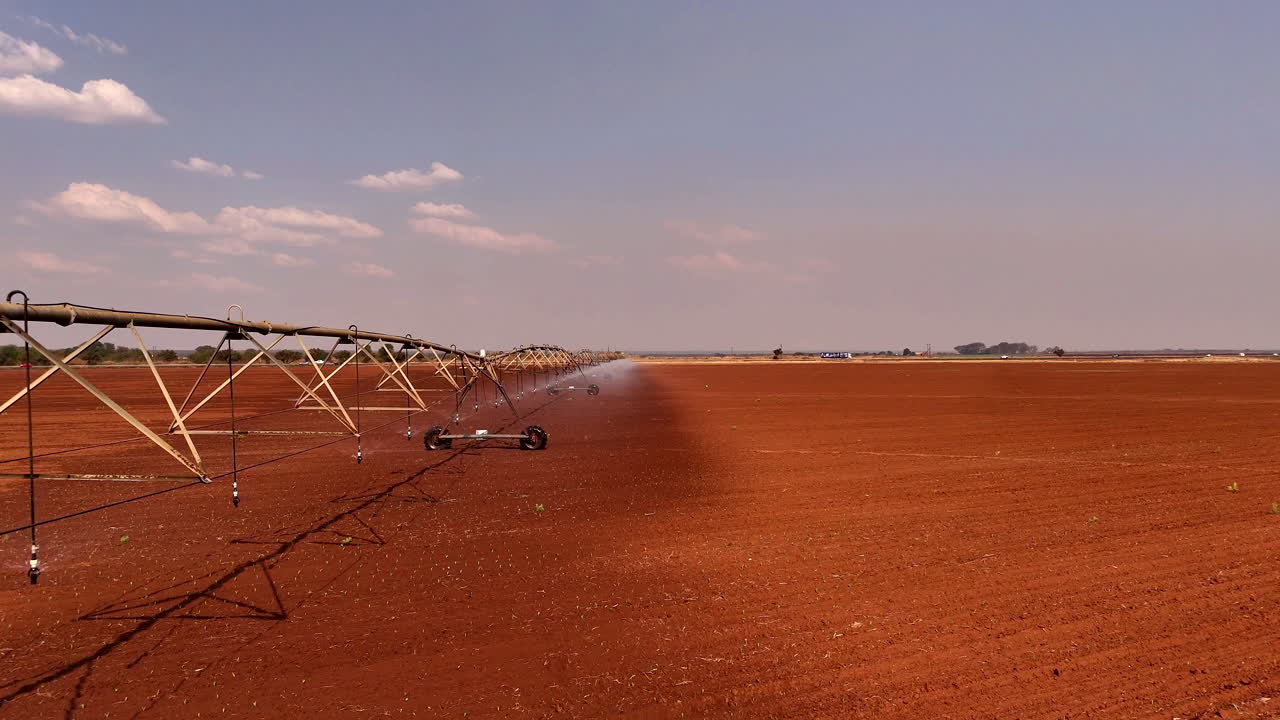 Center pivot irrigation system wetting freshly ploughed red soil on a dry farmland - drone footage