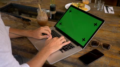 closeup de manos masculinas trabajando en una computadora portátil con pantalla verde en una cafetería