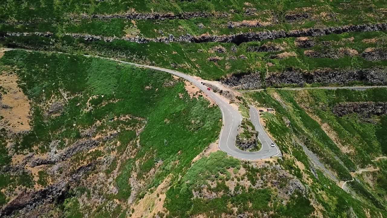 A breathtaking aerial view of winding mountain road at Miradouro Lombo do Mouro in Madeira. Surrounded by terraced green hills and rugged cliffs, this location highlights natural beauty and adventure