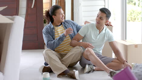 Happy-diverse-gay-male-couple-moving-into-new-home,-taking-selfies-in-living-room,-slow-motion