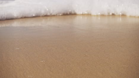 Close-up-of-white-foam-from-waves-washing-onto-yellow-sand-beach-shore