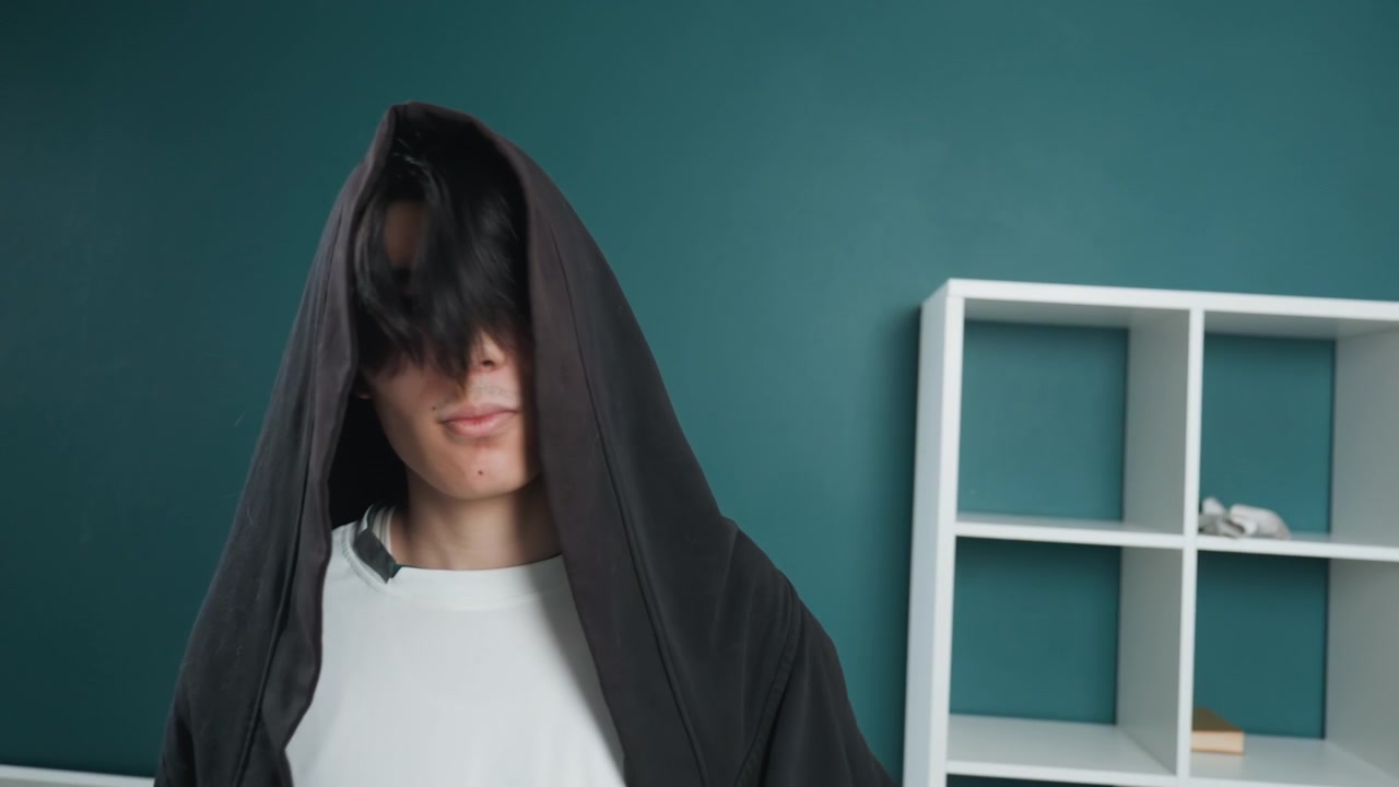 Hooded cleaner dusts teal shelves. Dramatic hooded figure wiping dusty home shelves with black cloak, slow sweeping motions, closeup portraits, minimalist interior, white cubed shelving, single potted