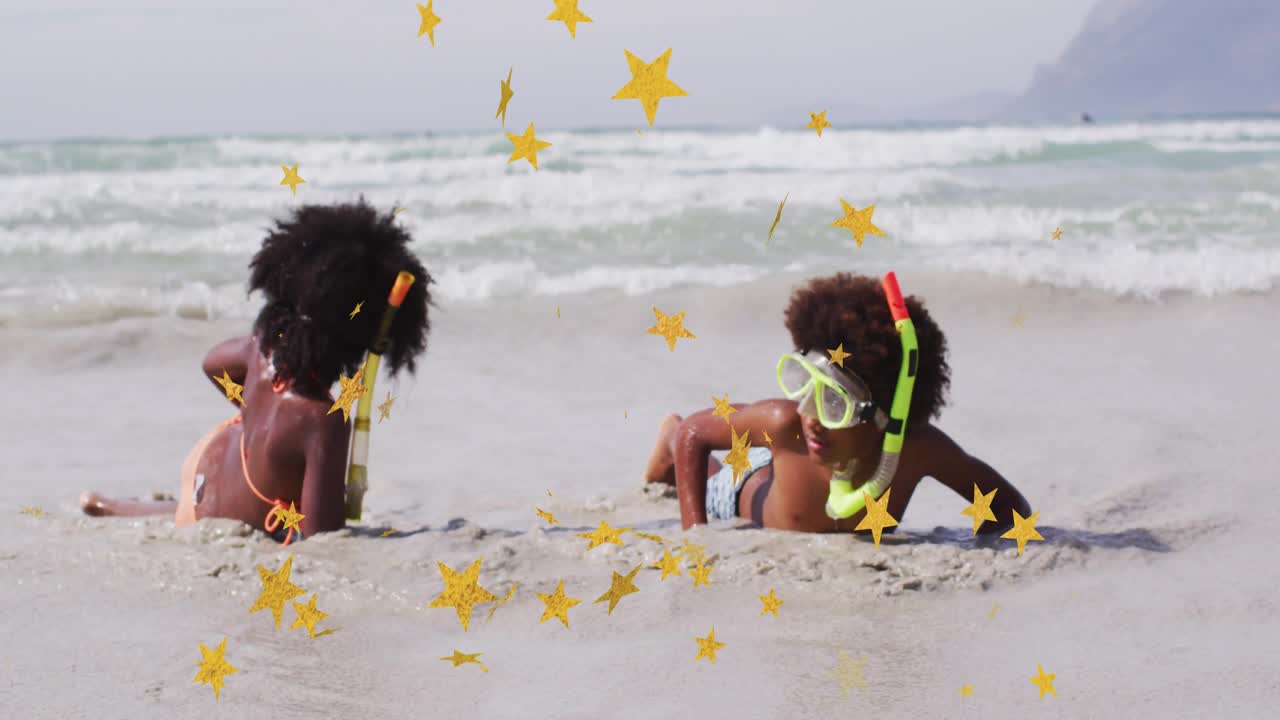 Due bambini sdraiati a riva, con le onde che li sfiorano, che giocano in una pubblicità di viaggio con una maschera al neon e stelle che fluttuano sopra di loro.