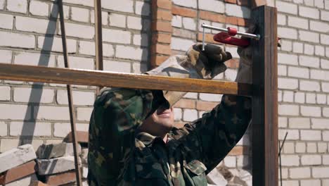 ein baumeister in handschuhen installiert eine klammer am zaun in der nähe eines backsteinhauses