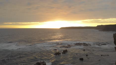 Aerial-shot-flying-right-in-between-the-two-peaks-of-eagles-nest-towards-the-sunset-on-the-Victorian-coastline