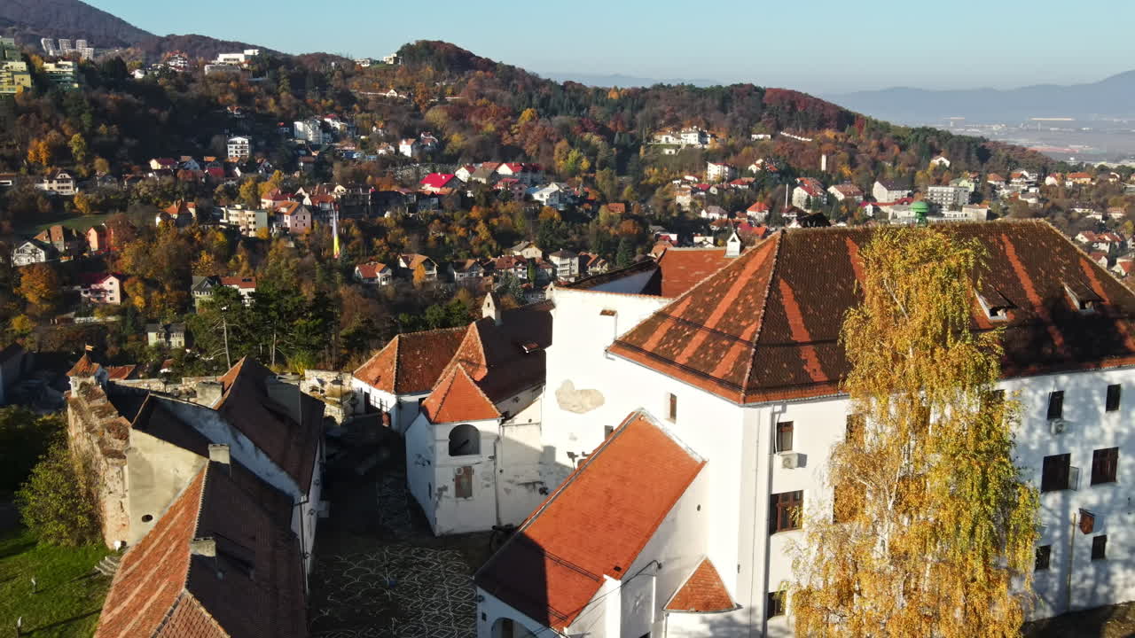 Aerial drone view of The Citadel in Brasov at sunrise, Romania. Medieval fortress on the top of a hill. Buildings, yellowed trees, tourists