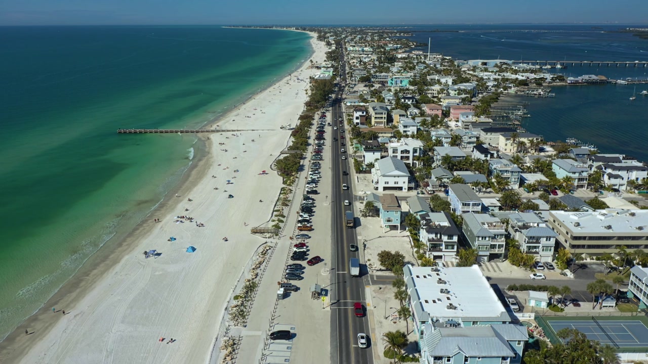 A bustling coastal road lined with parked cars, adjacent to a vibrant residential area and expansive ocean views. Ideal for urban planning or real estate visuals.