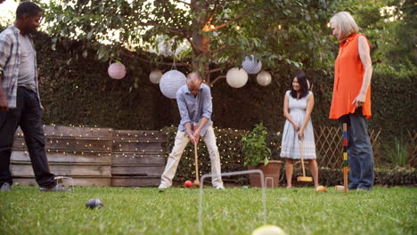 grupo de amigos maduros jugando al croquet en el patio trasero juntos