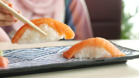 mujer comiendo sushi de salmón con palillos