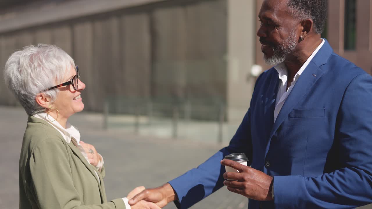 Mature businesswoman and african businessman shaking hands outdoors