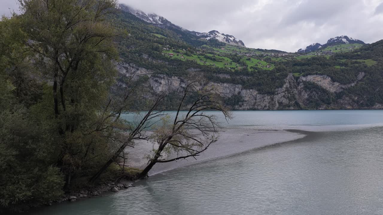 The silty river waters form a delta as they join the clear Walensee, set against the lower slopes of the Swiss Alps. Concept of hydrological dynamics and meeting of elements