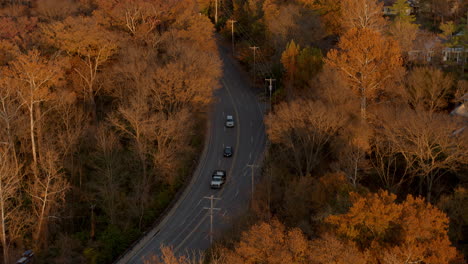 Antenne-über-Einer-Kurvenreichen-Straße-In-Der-Nähe-Einer-Kirche-Im-Herbst,-Während-Autos-An-Der-Kamera-Vorbeifahren,-Die-Nach-Unten-Geneigt-Ist