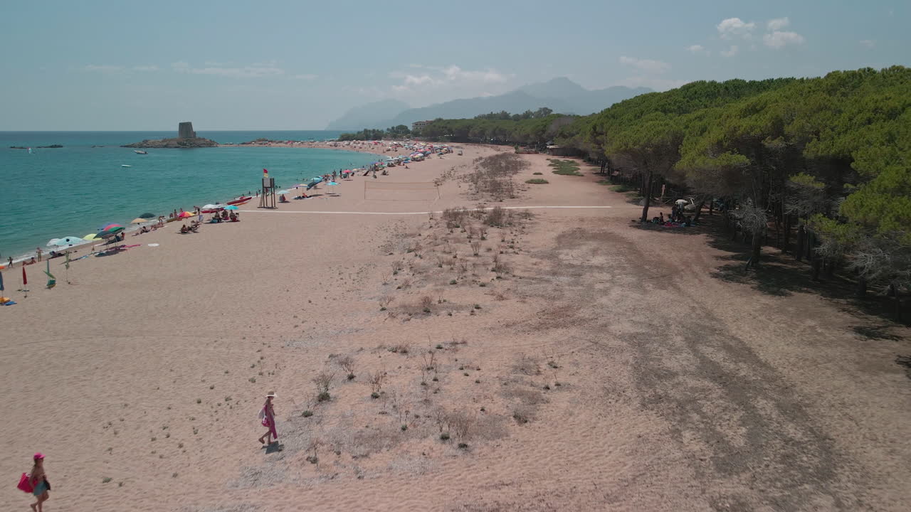 Slow Motion Of People Walking Towards Lush Forest Trees By The Beach On A Hot Sunny Weather. Emerald Coast In Sardinia, Italy. aerial drone