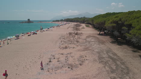 slow motion of people walking towards lush forest trees by the beach on a hot sunny weather. emerald coast in sardinia, italy. aerial drone