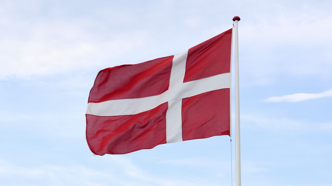 Dansk flag der blafrer i vinden med blå himmel i baggrunden.