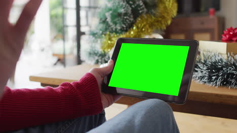 hombre caucásico en sombrero de santa haciendo llamada de video de navidad de tableta, con pantalla verde