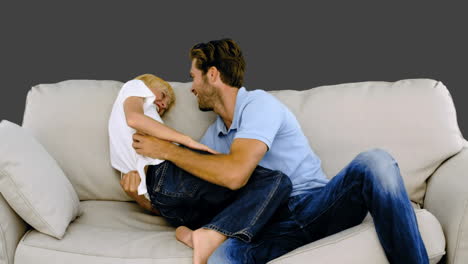 Father-tickling-his-son-on-the-sofa-on-grey-background