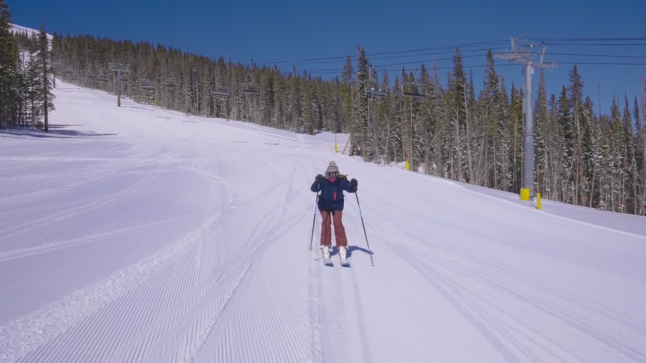 Sciatrice su una pista da sci battuta che usa i bastoncini per accelerare mentre supera una seggiovia.