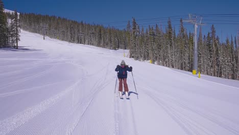 skier on a groomed ski resort trail using her ski poles to speed up while passing a ski lift