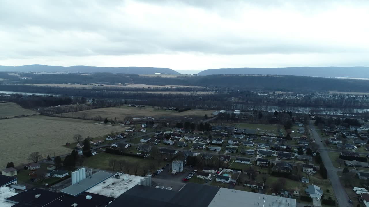 A drone shot above a city showing commercial buildings with a large green yard in front and residential houses stretching into the background