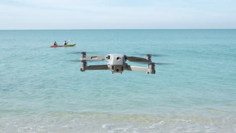 toma estática de un dron flotando en una playa con océano y kayakistas en segundo plano