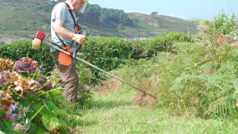 senior man in protective shield mask mowing grass with mower