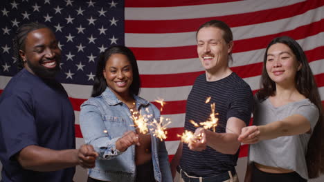 Studio-Portrait-Shot-Of-Multi-Cultural-Group-Of-Friends-Holding-Sparkler-Fireworks-In-Front-Of-American-Flag-Celebrating-4th-July-Independence-Day-3