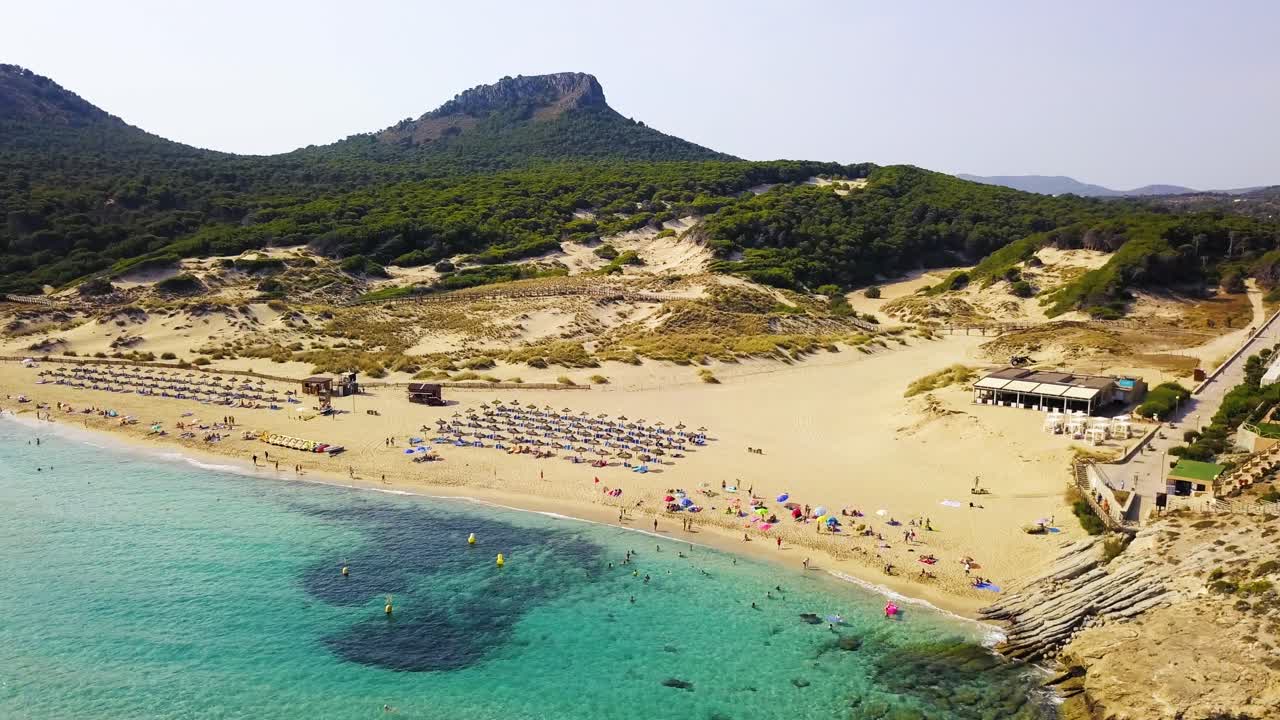Cala mesquida beach in mallorca with clear blue waters and busy sandy shores, surrounded by green hills, aerial view, Spain, in the Mediterranean Sea