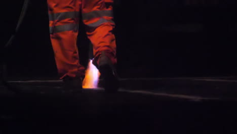 slow motion view of a road worker using a thermal lance to burn white lines from a main road before repainting at night