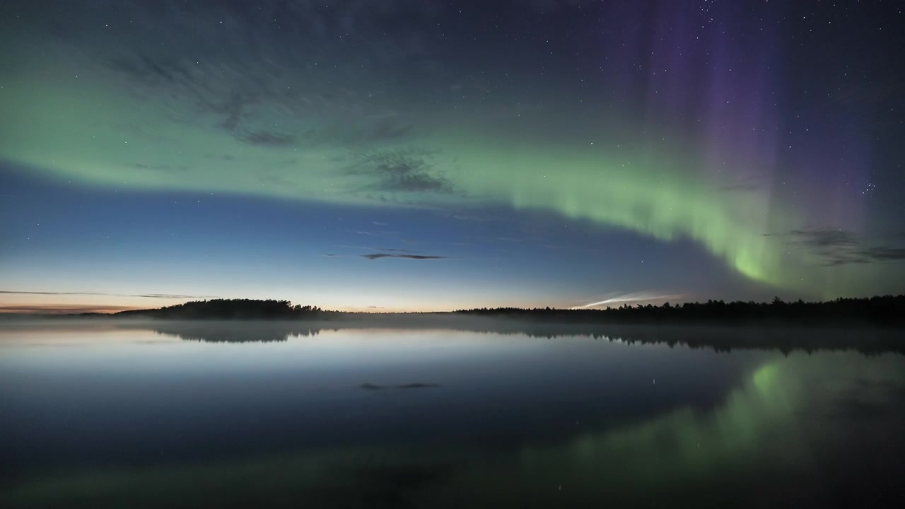 Timelapse av grönt och lila norrsken som speglas i en sjö