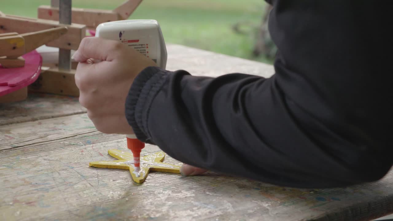 una niña esparce pegamento para madera en una estrella de madera aserrada y pintada