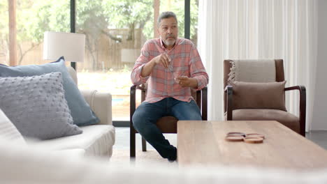 Worried-senior-biracial-man-sitting-in-armchair-thinking-in-living-room,-copy-space,-slow-motion