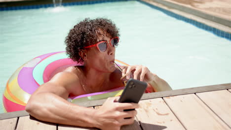 a young biracial man relaxes in a pool with a smartphone at home