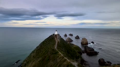 Drone-flying-to-Nugget-Point-Lighthouse,-popular-scenic-point-in-New-Zealand