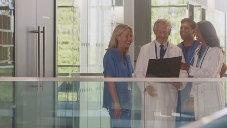 Multi-Cultural-Medical-Team-Wearing-White-Coats-And-Scrubs-Discuss-Patient-Scan-Meeting-In-Hospital