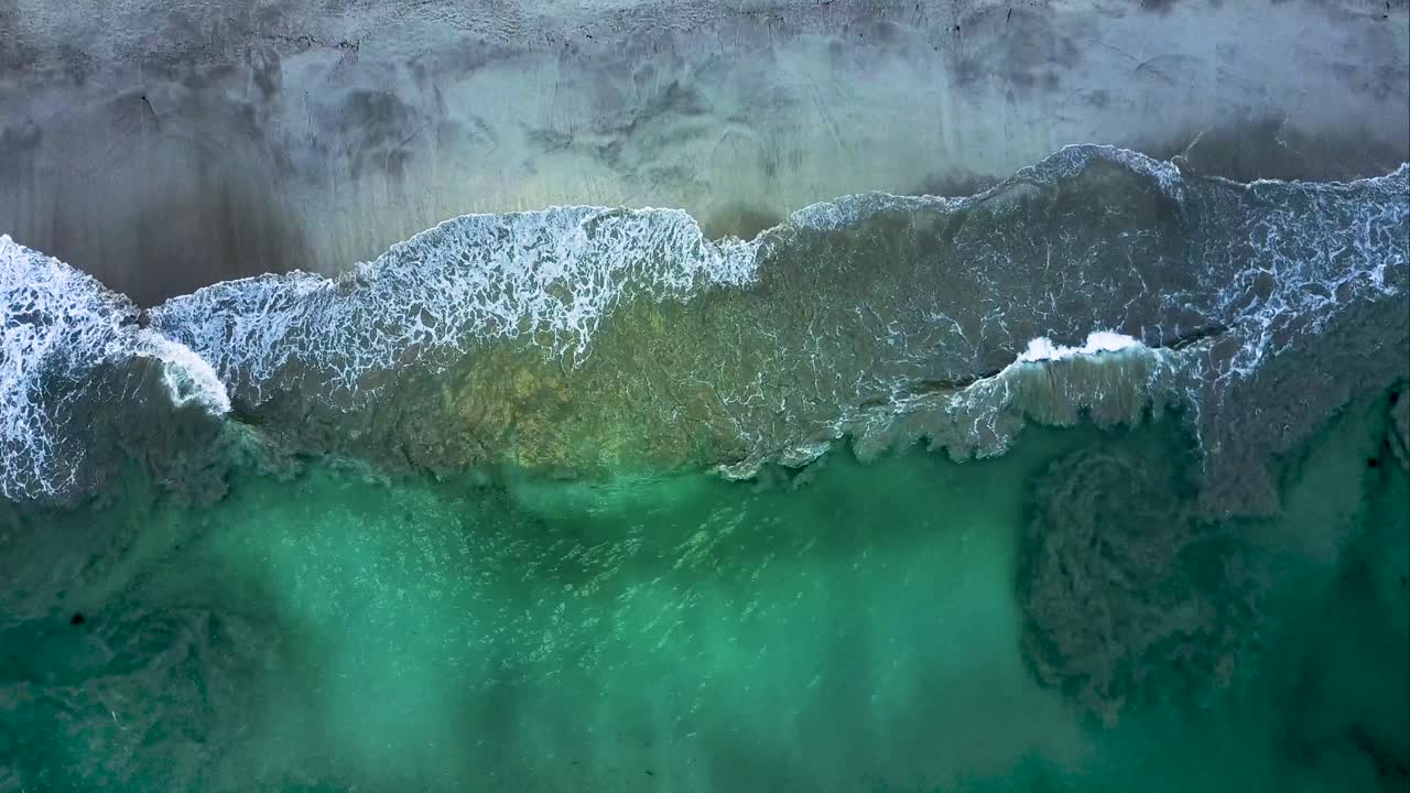 vista aérea de arriba hacia abajo de las aguas cristalinas de nueva zelanda con olas golpeando las costas de la playa de piha