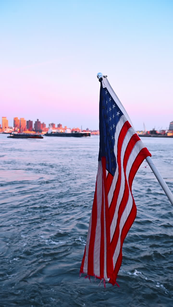 Bandiera americana che sventola sull'acqua. Una bandiera americana sventola nella brezza sopra l'acqua al crepuscolo, con lo skyline di una città sullo sfondo