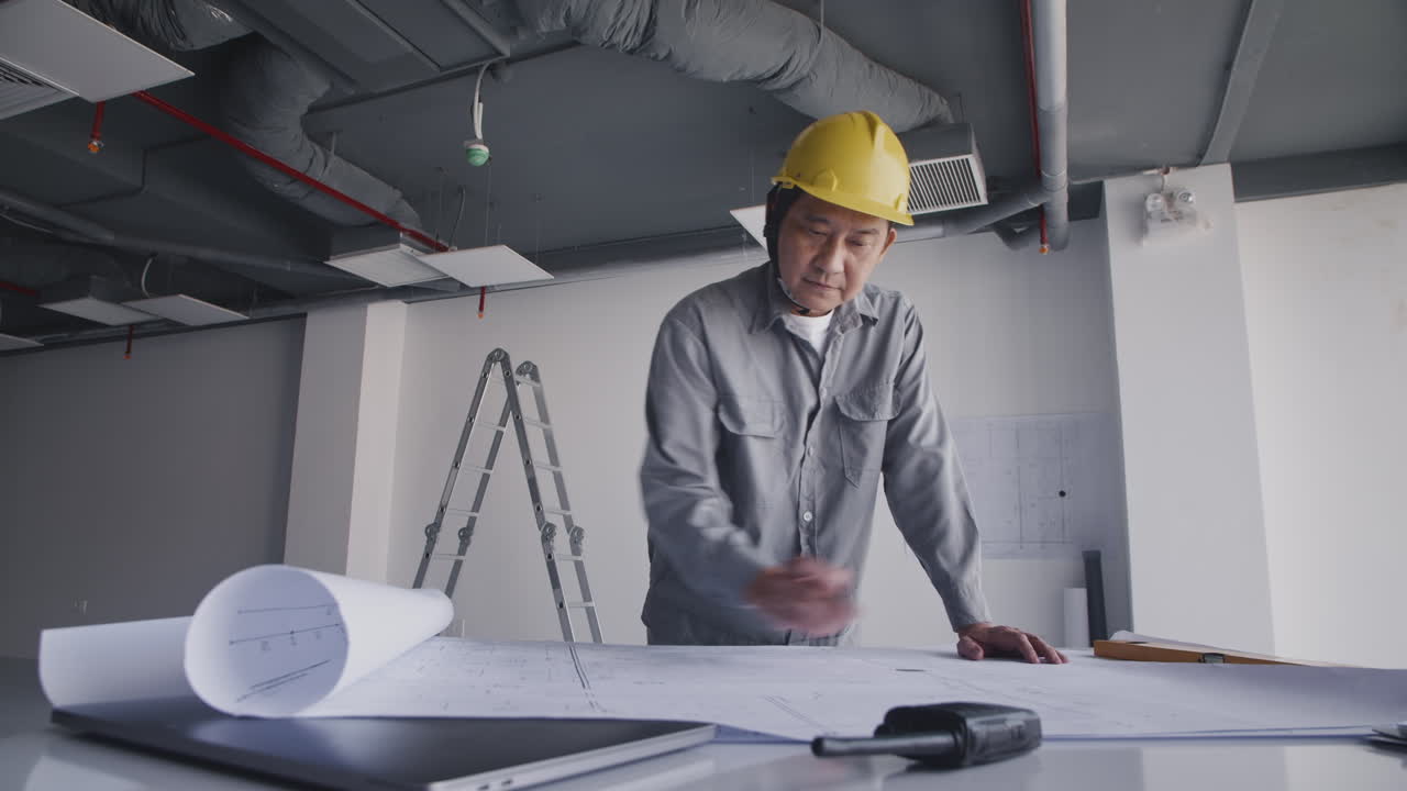 Asian Engineer Planning Details of Room on Blueprint