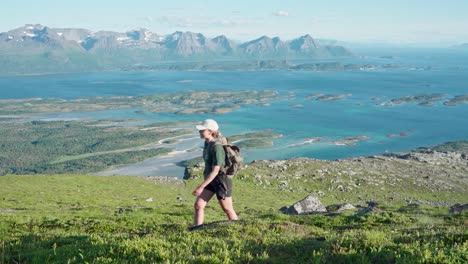 female hiker crossing the meadow with view of the ocean in norway